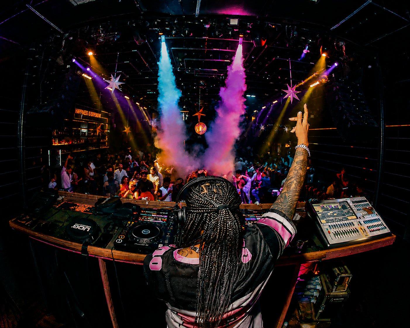 DJ Kim at the decks, arm raised, as CO2 jets fire over a full floor