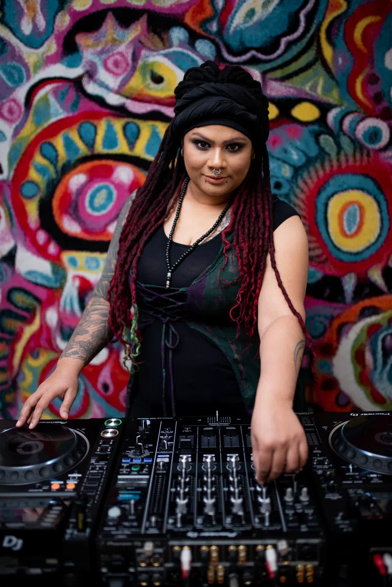DJ Kim standing behind a DJ mixer in front of a colourful mural