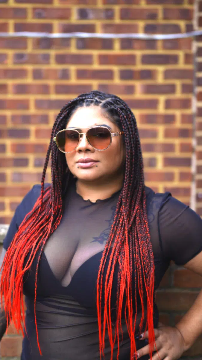 DJ Kim wearing sunglasses in a portrait against a brick wall