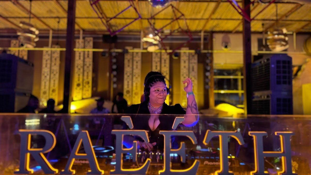 DJ Kim at the decks behind the Raeeth booth sign, Goa